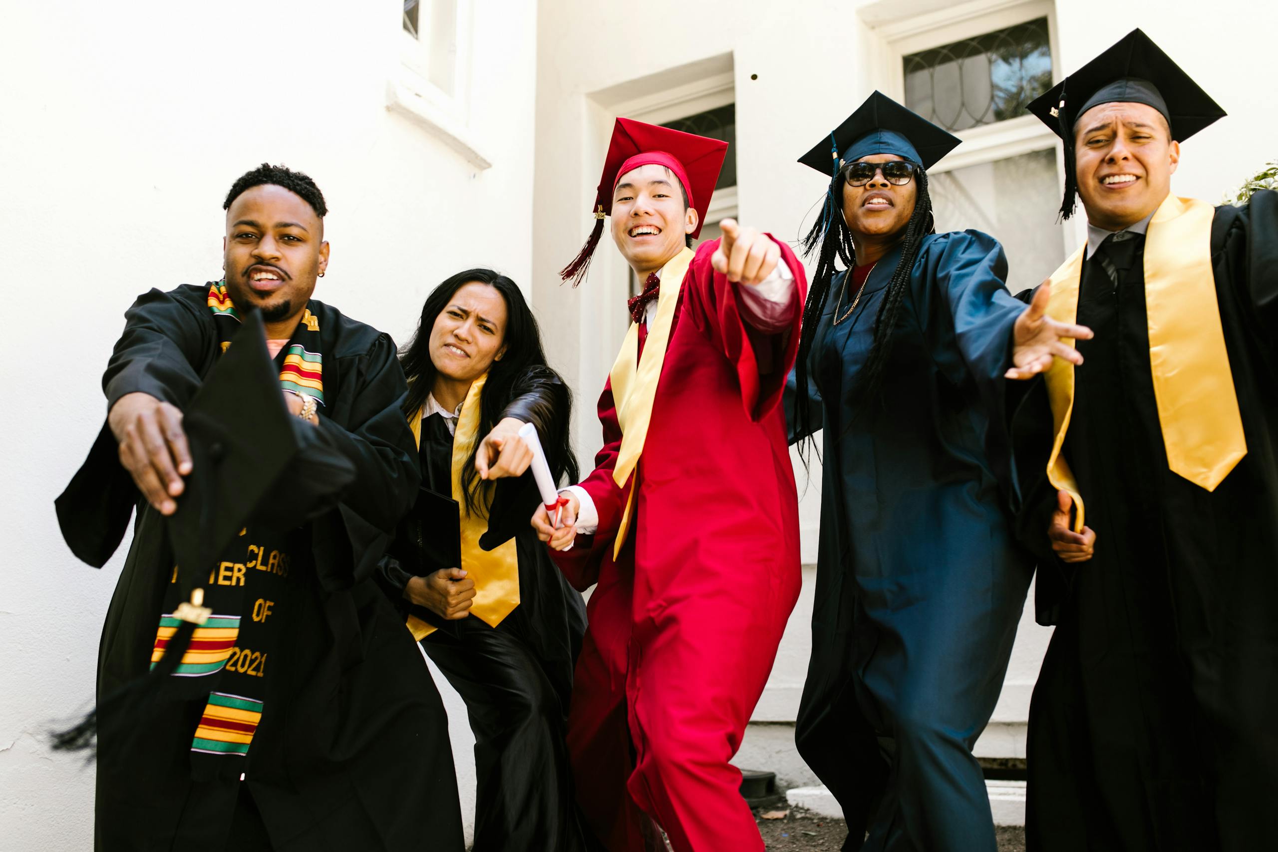 Cheerful graduates celebrating their success in colorful gowns outdoors.